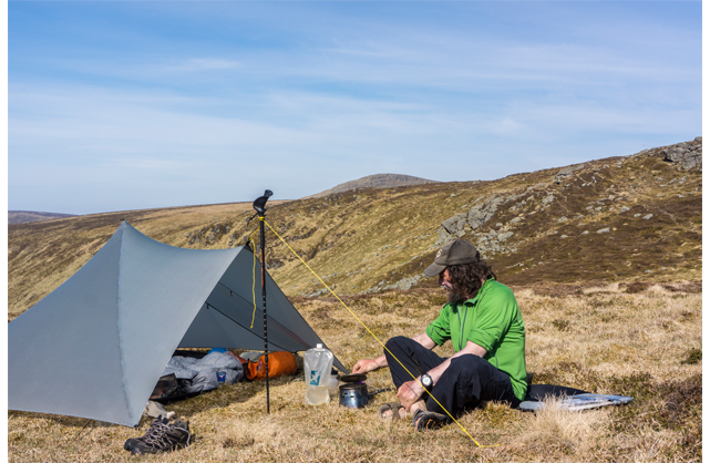 Man in green sat next to pitched, grey Mountain Laurel Designs Trailstar Shelter