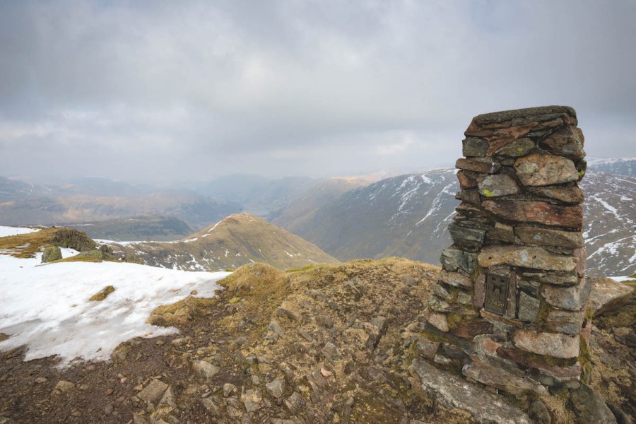 Stone tower marker at the Red Screes summit, a great dog-friendly walk in the Lake District, with cloud covered mountains behind