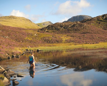 Woman in blue swimsuit wading into lake to wild swim