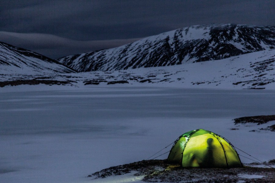 Glowing green tent in dark snowy mountains