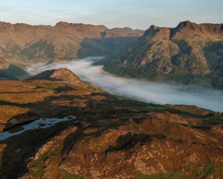 Aerial view of Langdale Valley and the Langdale Pikes in the Lake District National Park. A layer of mist can be seen below the mountains on this beautiful late Summer morning.