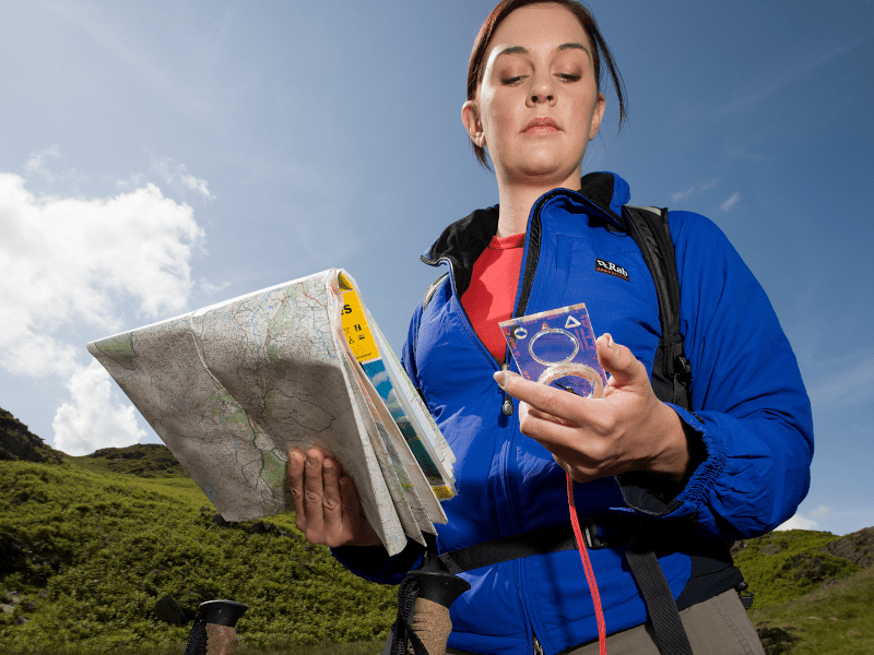 Woman reading a compass while holding a map.