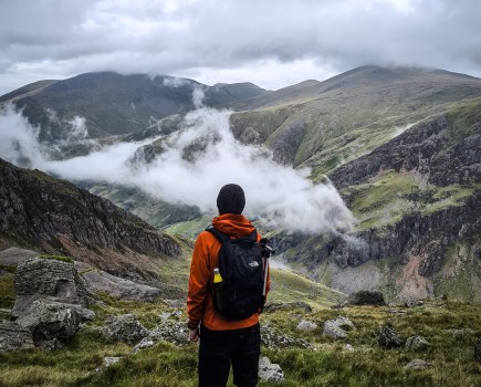A hiker standing in Snowdonia wearing one of the different types of backpack