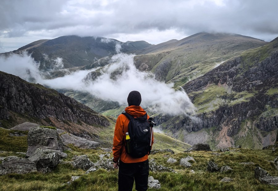 A hiker standing in Snowdonia wearing one of the different types of backpack