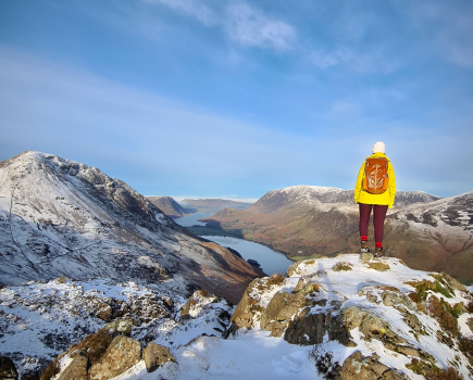 A walker looks down on Buttermere in the Lake Distrcit wearing a regular backpack for hiking