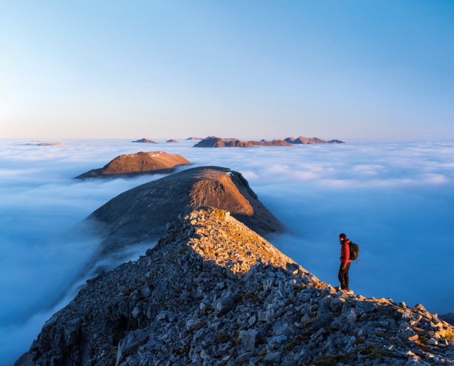Man standing on top of mountain looking out above the clouds