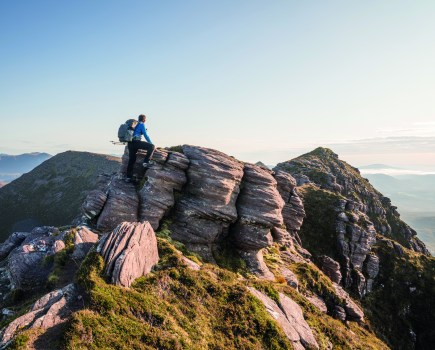 A walker stands atop Ben Mor Coiagach carrying one of the many different types of backpacks on the outdoor gear market.