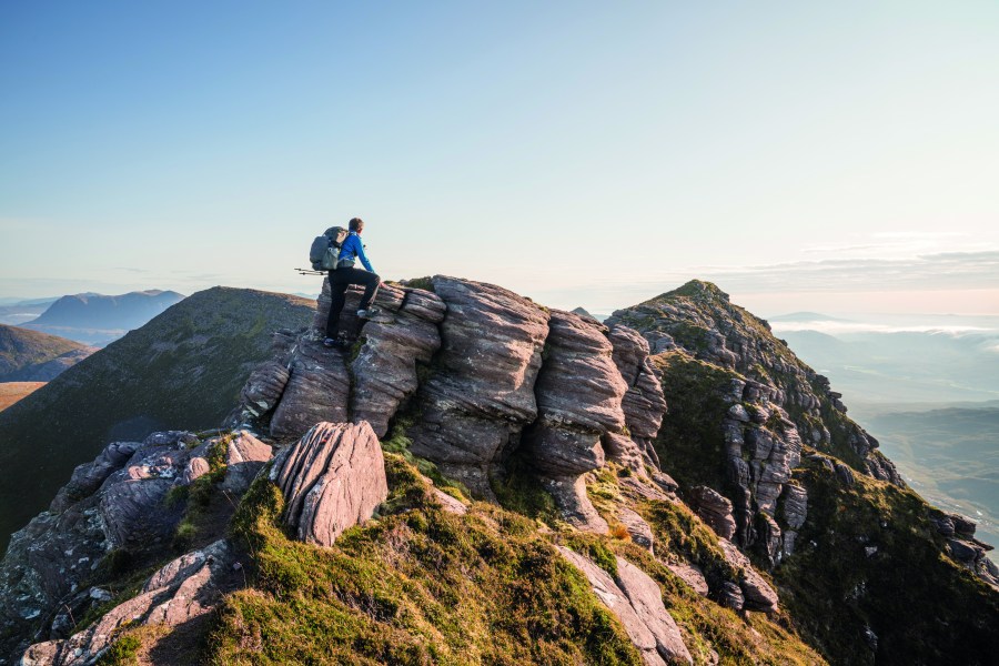 A walker stands atop Ben Mor Coiagach carrying one of the many different types of backpacks on the outdoor gear market.