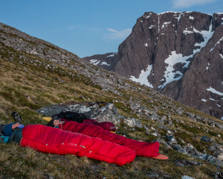 A couple on the side of a mountain looking up at the sky in red sleeping bags
