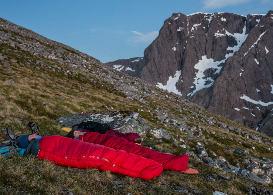 A couple on the side of a mountain looking up at the sky in red sleeping bags