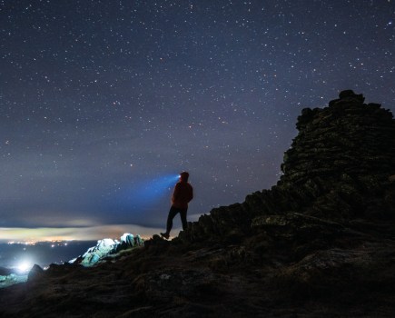 The best head torches for hiking. Man standing on a mountain night is falling and you can see that his head torch is on