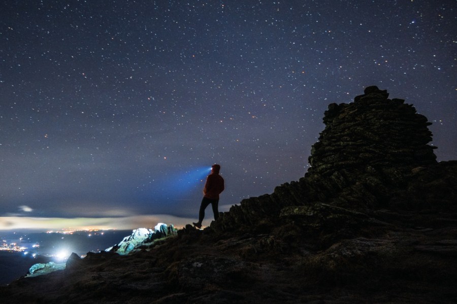 The best head torches for hiking. Man standing on a mountain night is falling and you can see that his head torch is on