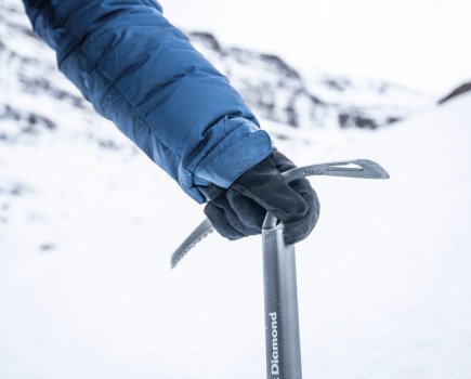 Someone holding a ice axe in the snow with winter gloves on