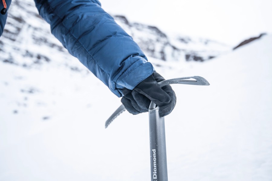 Someone holding a ice axe in the snow with winter gloves on