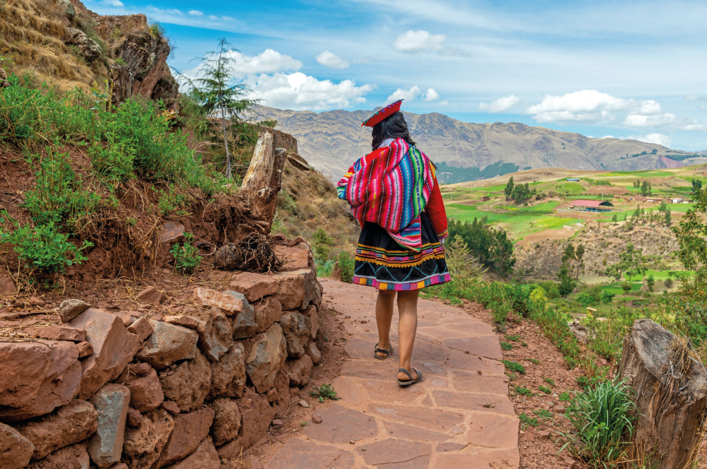 Indigenous peruvian quechua woman in traditional textile clothing walking on inca trail, Sacred valley, Cusco, Peru.