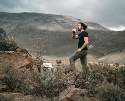 a man in black shirt standing while drinking coffee near the mountain