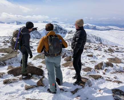 Hikers pointing out Ben Macdui from the snowy summit of Cairn Gorm