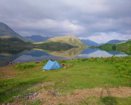 Bright blue tent constructed beside Loch Arkaig with mountains in background
