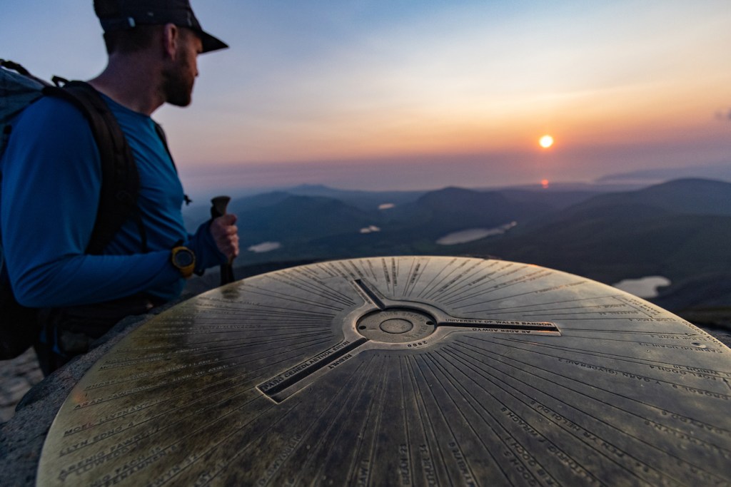 Close up of the Snowdon Summit, a copper looking circle table with engravings with an orange sunset behind
