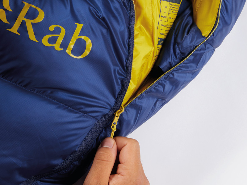 Close up of a hand unzipping the front main zip of Rab Neutrino sleeping bag, blue and yellow