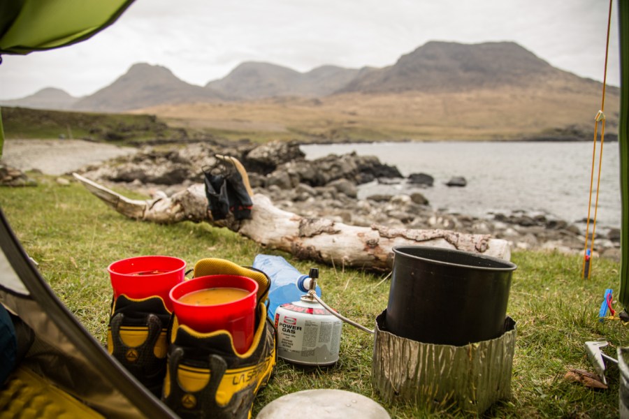 Gas cooker and shoes holding pots of soup outside tent next to lake