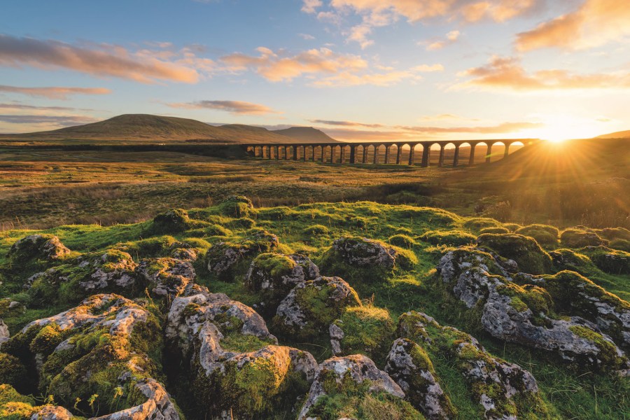 Golden sun over tall bridge arches with three peaks beyond