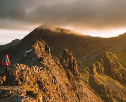 Hiker in red jacket walking along golden brown mountain tops