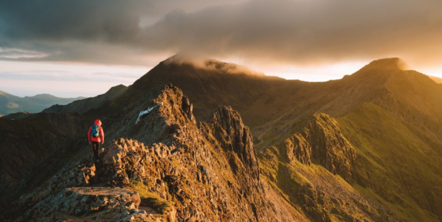 Hiker in red jacket walking along golden brown mountain tops