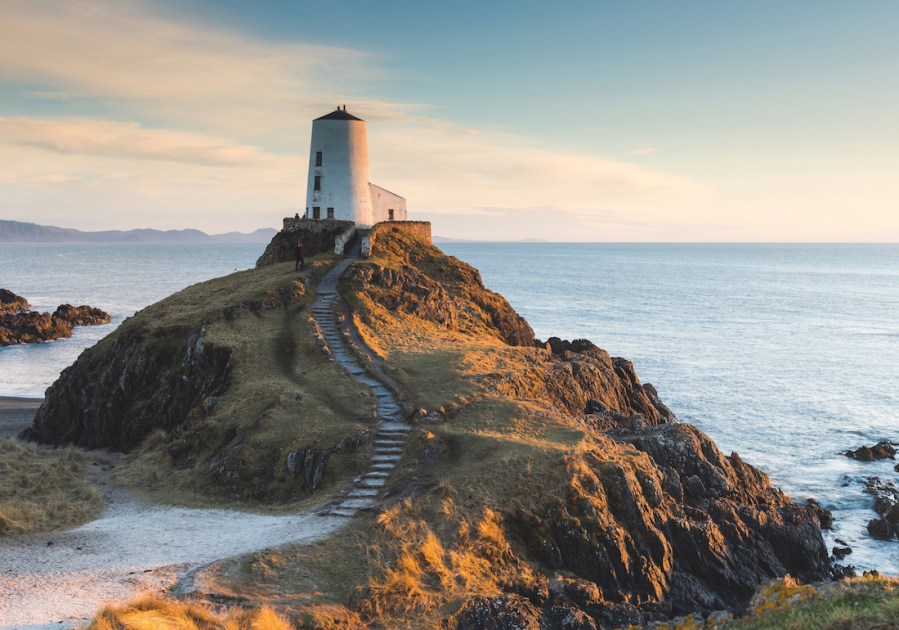 Lighthouse Ynys Llanddwyn on a mound above the sea with a grey stone staircase and rocky coastal terain